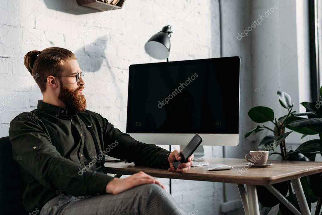 handsome businessman sitting, holding smartphone and looking away