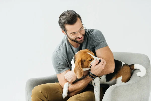 白で隔離の肘掛け椅子に犬と遊んで笑顔のハンサムな男 — ストック写真