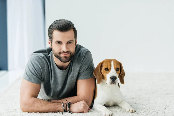 Schöner Mann Liegt Mit Niedlichem Beagle Auf Teppich Und Schaut — Stockfoto