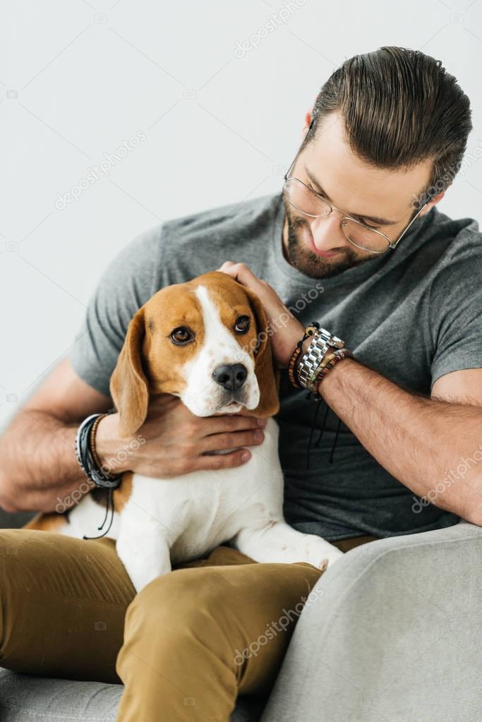 smiling handsome man palming dog on armchair isolated on white