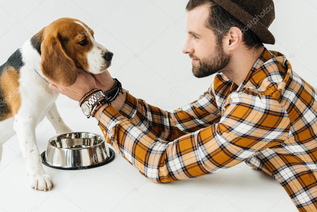 side view of man palming dog at table with pet bowl