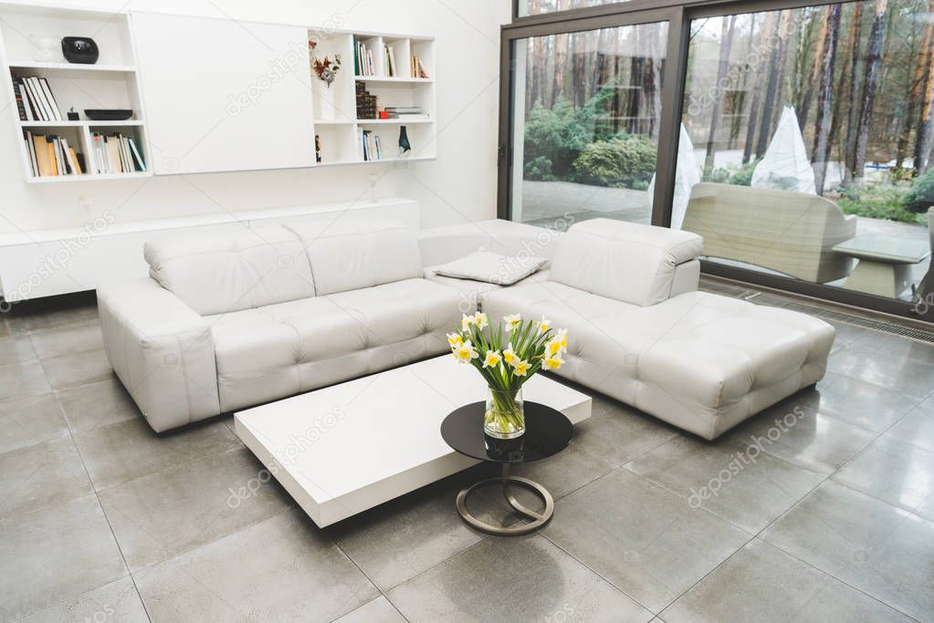 view of empty living room with white sofa and bouquet of flowers on coffee table