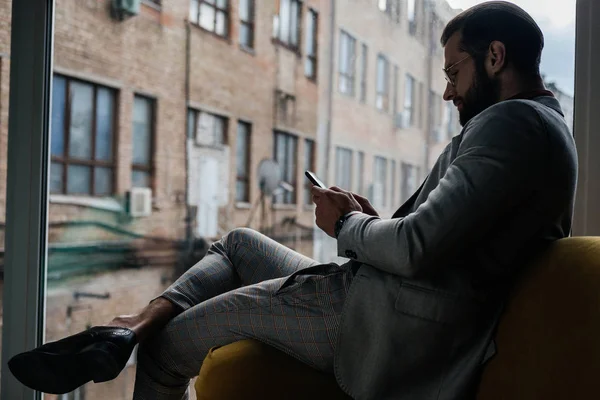Stylowe Człowieka Pomocą Smartfona Siedzi Przy Oknie — Zdjęcie stockowe