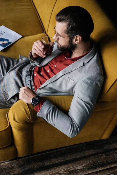 Eleganter Mann Trinkt Whiskey Und Sitzt Mit Zeitung Auf Sofa — Stockfoto