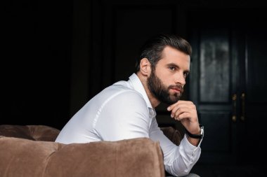 thoughtful handsome bearded man sitting in armchair clipart