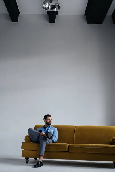 Stylowy Mężczyzna Niebieskim Modny Garnitur Pomocą Smartfona Siedzi Kanapie Żółty — Darmowe zdjęcie stockowe
