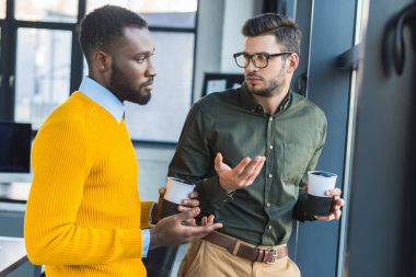 multicultural businessmen talking during coffee break in office clipart