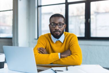 african american businessman sitting with crossed arms and looking at camera in office