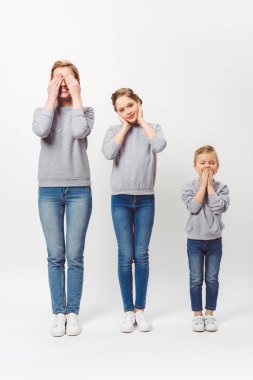 mother and daughters of different generations in similar clothing covering parts of faces isolated on grey clipart
