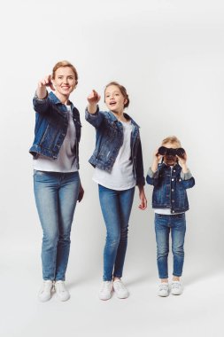 daughter and mother pointing away while little sister with binoculars looking away isolated on grey clipart
