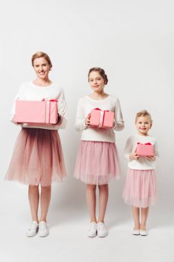 smiling mother and little daughters in similar pink tutu tulle skirts with wrapped gifts isolated on grey clipart
