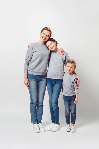 mother and daughters of different generations in similar clothing hugging each other isolated on grey