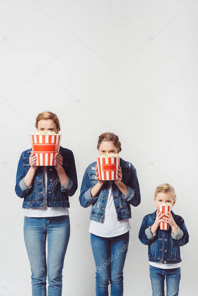 obscured view of family in similar denim clothing covering faces with popcorn isolated on grey