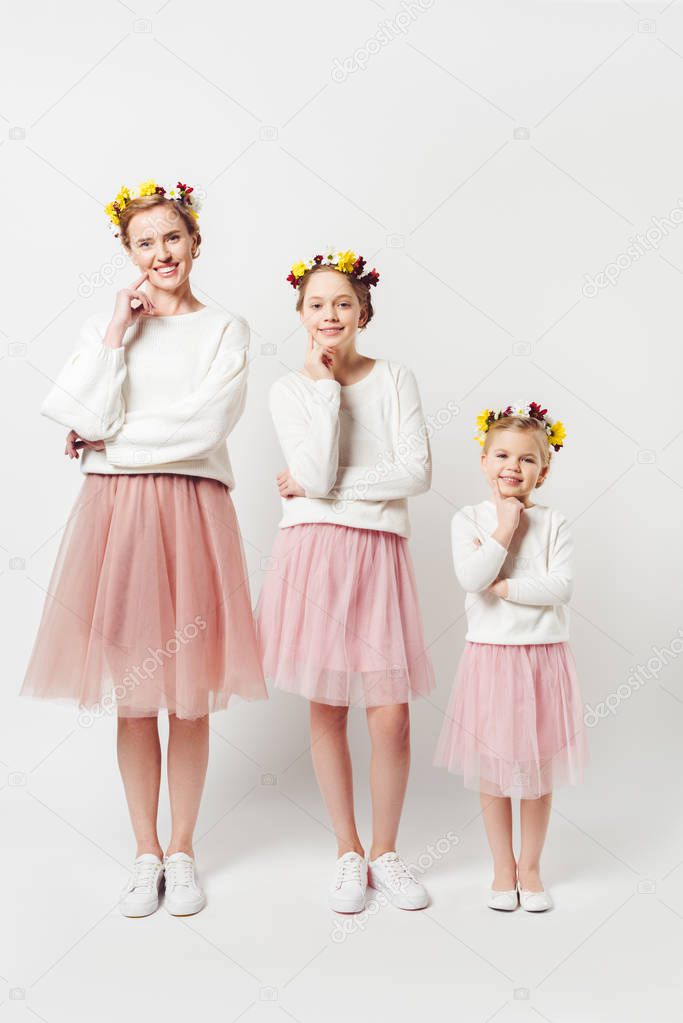beautiful mother and daughters in similar clothing with floral wreathes on heads isolated on grey