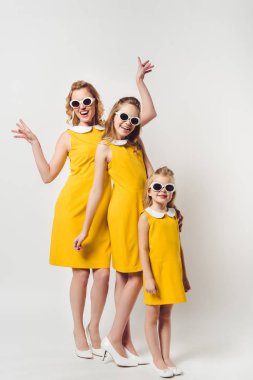 Mutlu anne ve kızlar benzer geçmişe dönük sarı elbiseler giyiyorlar.