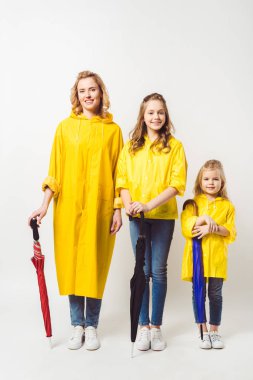 mother and daughters in yellow raincoats with umbrellas on white clipart