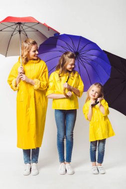 happy mother and daughters in yellow raincoats with umbrellas on white clipart