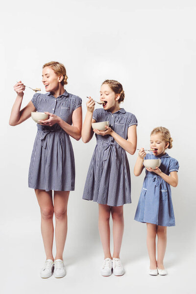 mother and daughters in similar dresses eating cereal breakfast together on white