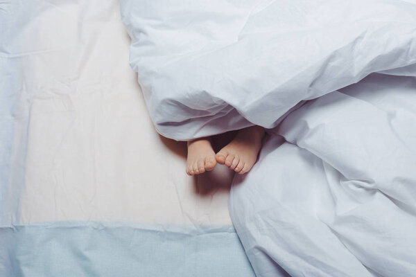 cropped shot of child feet underneath blanket 