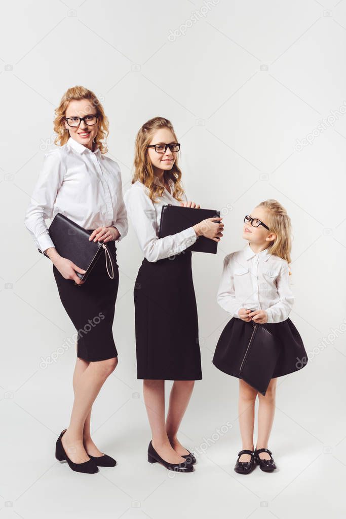 mother and daughters in similar businesswomen costumes with clutches on white