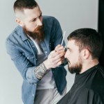 Zijaanzicht van Kapper snijden klant haren op barbershop geïsoleerd op wit