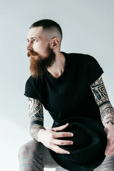 Handsome Bearded Tattooed Man Holding Hat Looking Away White — Stock Photo, Image