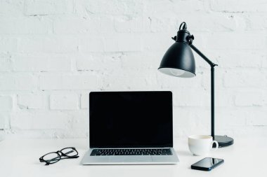 Boş ekran, smartphone, lamba ve masa üzerine gözlük ile dizüstü bilgisayar 