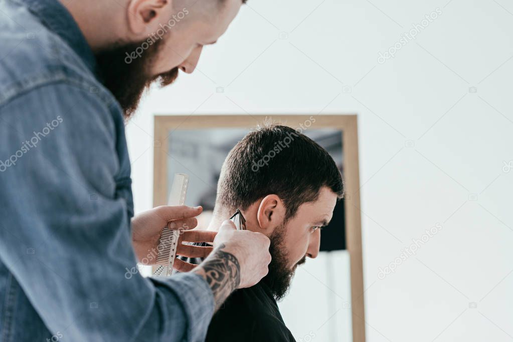 side view of barber shaving customer hair at barbershop isolated on white