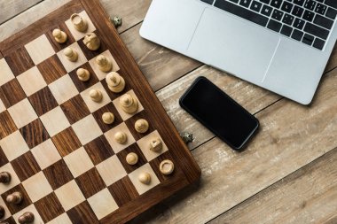 Akıllı telefon, laptop ve satranç kurulu satranç taşları tahta yüzeyi ile