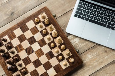 Laptop and chess board with figures on rustic wooden surface clipart