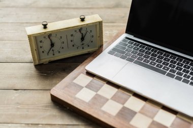 Chess clock, laptop and chess board on rustic wooden surface clipart