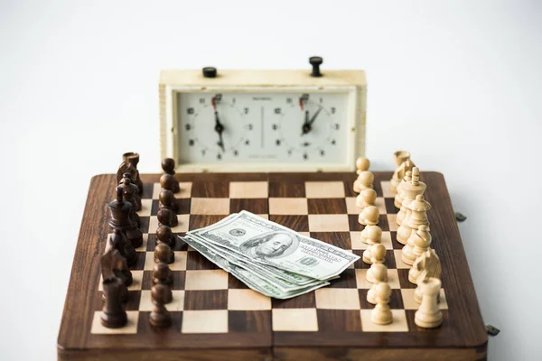 Chess clock near chess board with figures and dollar banknotes isolated on white