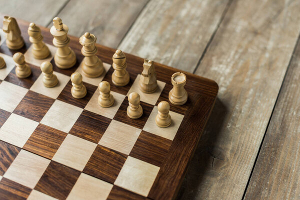 Cropped view of chess board with white chess pieces on rustic wooden surface