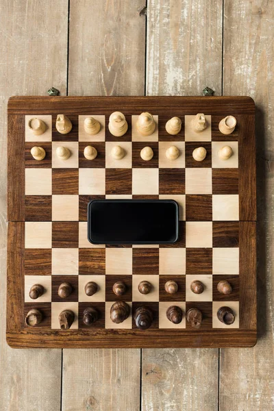 木の表面にスマート フォンとチェスの部分とのチェス盤の上から見る — ストック写真