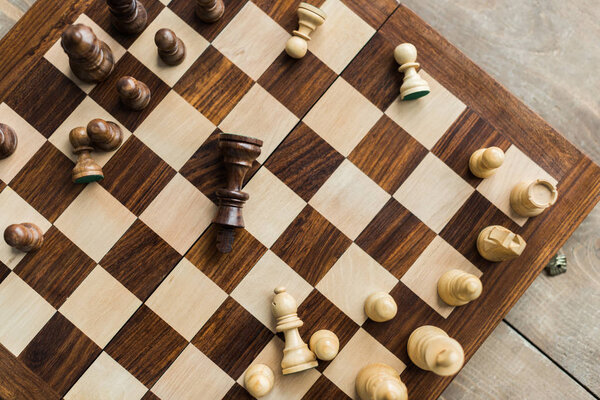 Chess board with scattered chess figures on wooden surface