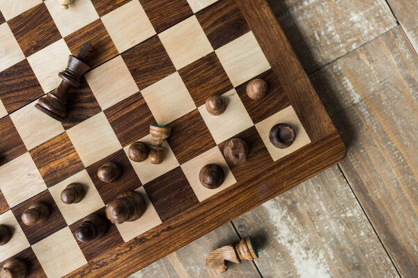 Top view of chess board with scattered black chess pieces on rusitc wooden surface