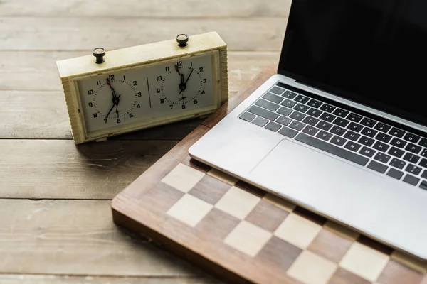 国际象棋时钟 笔记本电脑和棋盘上的仿古木表面 — 图库照片
