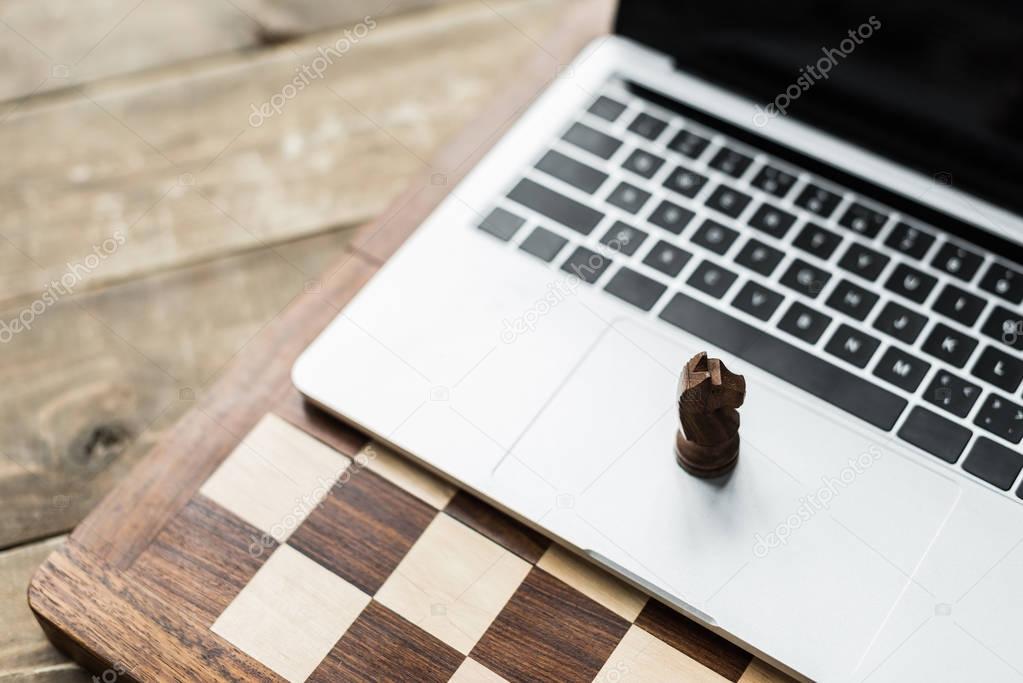 Close up of chess board and laptop with chess figure of knight  