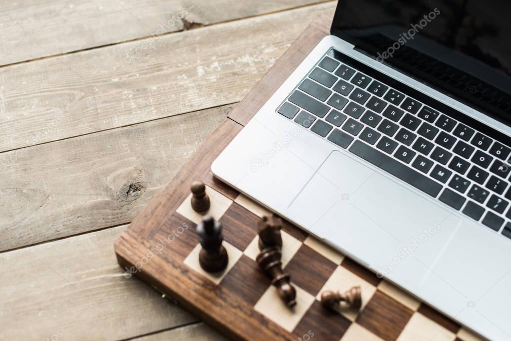 Chess board with chess pieces and laptop on rustic wooden surface