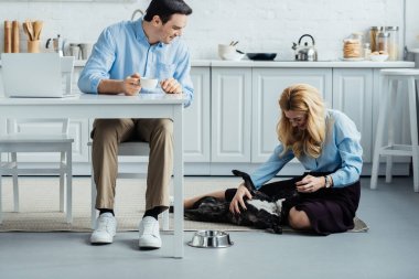 Kahve tablo ile laptop mutfak ve Fransız köpek okşayarak sarışın kadın tarafından ile gülümseyen adam