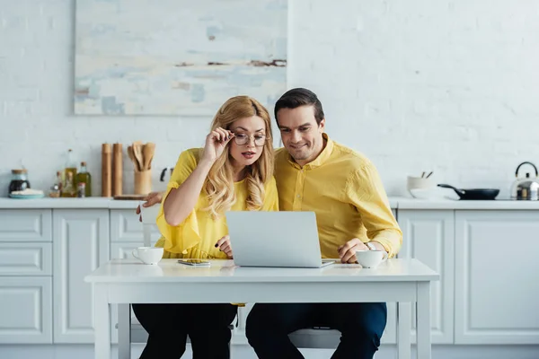 兴奋夫妇喝咖啡 看笔记本电脑屏幕厨房表 — 图库照片