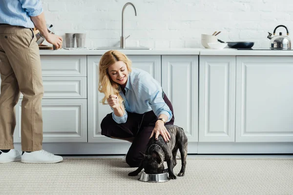 男子酿造咖啡和金发女郎抚摸法国斗牛犬在厨房地板上 — 图库照片