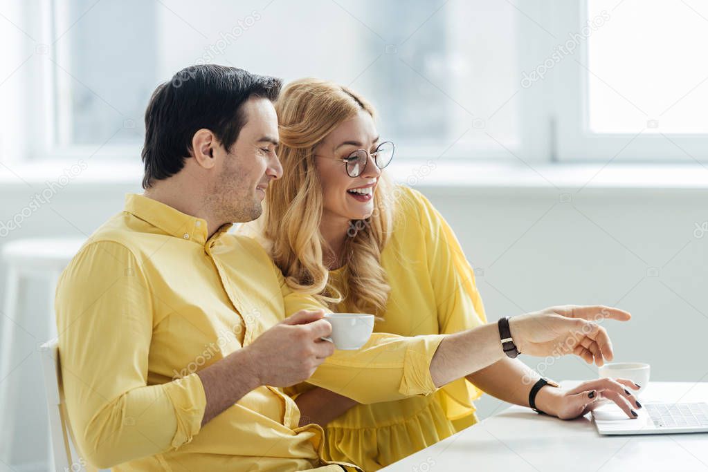 Couple drinking coffee and talking by table with laptop