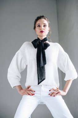 güzel genç kadın şık kıyafeti ile el HIPS ve gri kameraya bakarak otururken
