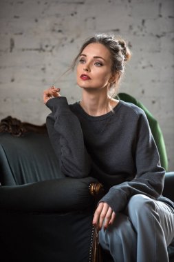 çekici esmer kadın olarak koltukta oturan ve uzağa bakarak trendy jumper