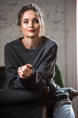 koltukta oturan ve kameraya gülümseyen gri süveterli çekici esmer kadın portresi 