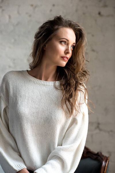 portrait of beautiful young brunette girl in trendy white sweater looking away