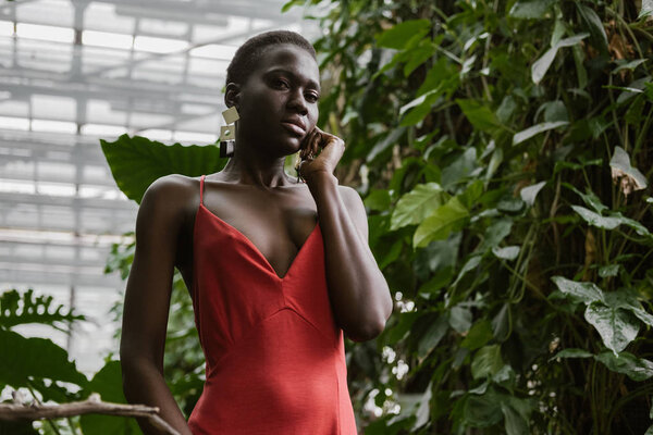 elegant african american girl posing in red dress in tropical garden