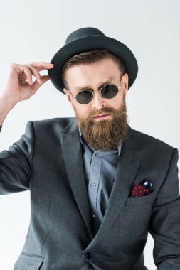 Şapka ve güneş gözlüğü üzerinde ışık arka plan izole giymiş şık sakallı adam