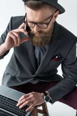 Yakışıklı işadamı smartphone üzerinde konuşmak ve açık renkli izole laptop çalışma vintage tarzı giysiler